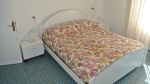 Un dormitorio con una cama, una mesita de noche, una lámpara y un enchufe.