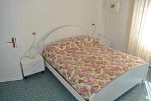 Ein Schlafzimmer mit einem Bett, einem Nachttisch, einer Lampe und einer Steckdose.