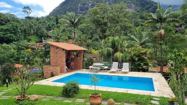 A swimming pool with a brick structure, surrounded by lush greenery and a mountain backdrop. - Apartment with kitchenette, 2 bedrooms and private bathroom. (Teresópolis)