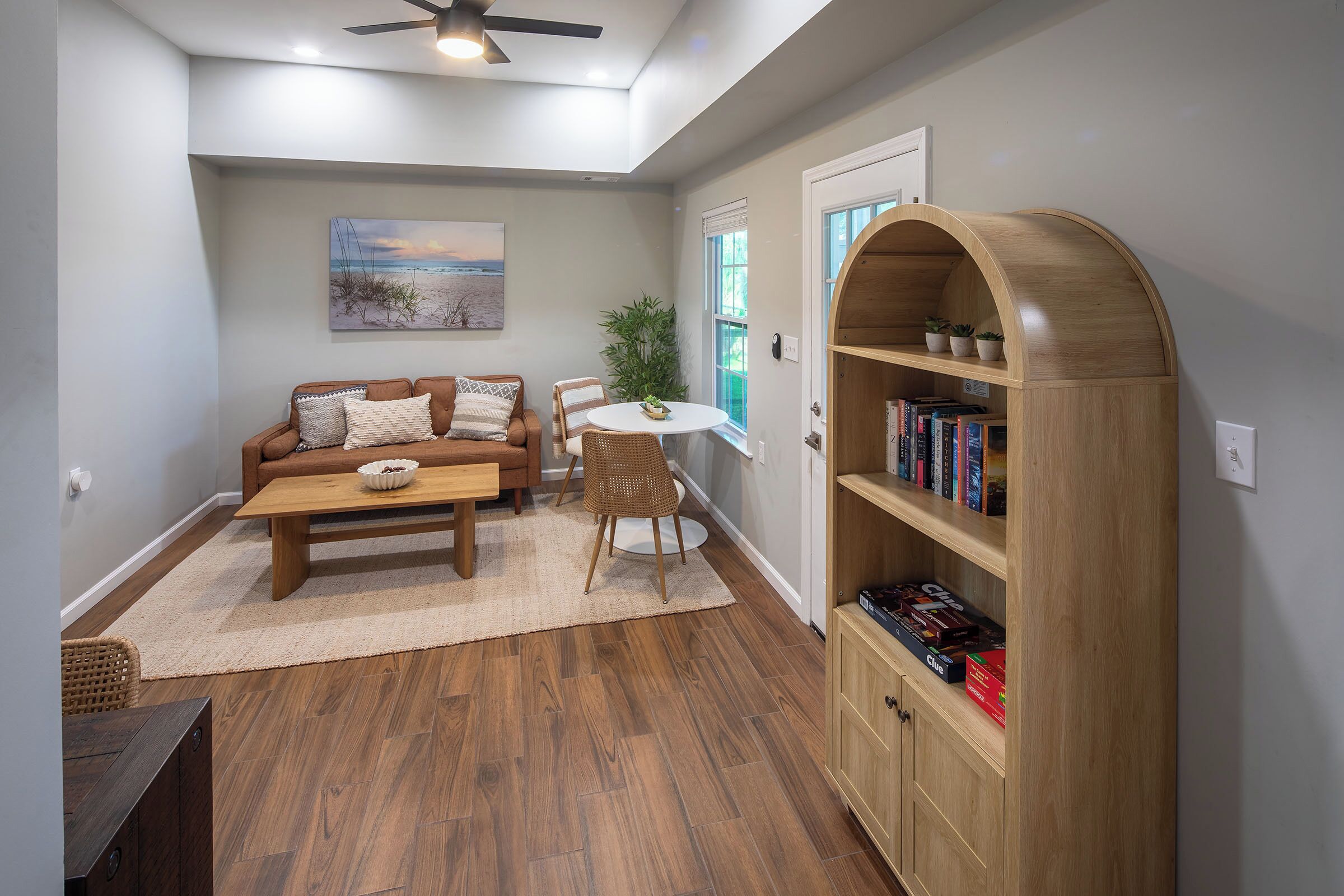 A living room with a brown sofa, a coffee table, a bookshelf, and a ceiling fan.