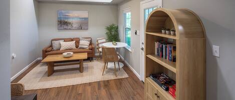 A living room with a brown sofa, a coffee table, a bookshelf, and a ceiling fan.