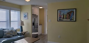 Ein Wohnzimmer mit einer Couch, einem Tisch, einer Lampe, einem Kühlschrank und einem Bild an der Wand.