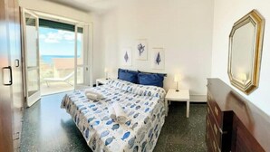 Une chambre à coucher comprenant un lit, une table de chevet, une commode, une fenêtre donnant sur un paysage agréable et une porte.