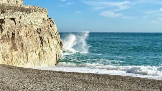 Une falaise côtière où les vagues s’écrasent, un ciel dégagé et une mer calme.