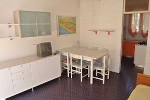 Ein Zimmer mit einem weißen Tisch, Stühlen, einem Fernseher, einer Karte an der Wand und einer Küchenzeile.