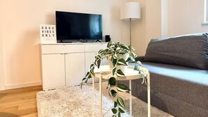 Una sala de estar con televisor de pantalla plana, una planta en maceta, una lámpara y un sofá.