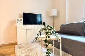 Ein Wohnzimmer mit Flachbildfernseher, einem Blumentopf, einer Lampe und einem Sofa.