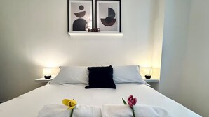 Una cama bien hecha con sábanas blancas, un almohadón negro y dos lámparas de noche.
