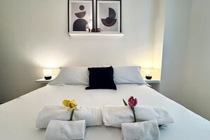 Ein ordentlich bezogenes Bett mit weißen Leinen, einem schwarzen Kopfkissen und zwei Nachttischlampen.