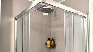 Un baño moderno con cabina de vidrio, ducha de mano y estante con artículos de aseo.