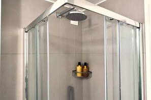 Eine moderne Dusche mit Glastrennwand, Duschbrausehandstück und Ablage für Pflegeprodukte.
