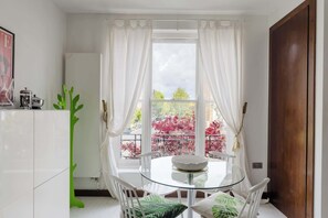 Ein Essbereich mit einem Glastisch, weißen Stühlen und Blick auf einen Balkon mit rotem Laub.