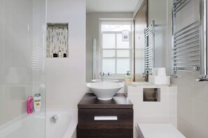 A modern bathroom with a large mirror, a bathtub, a sink, and a shower. - Chic 2BDR East London Hideaway (Greater London)