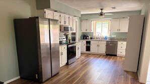 Una cocina con suelo de madera, armarios blancos, electrodomésticos de acero inoxidable y un ventilador de techo.