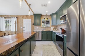 Eine Küche mit grünen Schränken, Edelstahlgeräten, einer Holz Arbeitsplatte und Pendelleuchten.