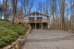 Ein zweistöckiges Haus mit einem Steinsschornstein, einer Holzterrasse und einer Auffahrt mit Kies.