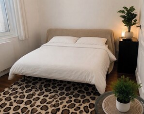 Ein Schlafzimmer mit einem Bett, einem Leopardenfellteppich, einem Nachttisch mit Lampe und einer Topfpflanze.