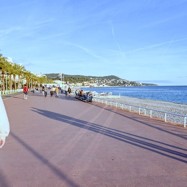 Eine Küstenpromenade mit gepflastertem Gehweg, Bänken und einem Geländer mit Blick auf das Meer.