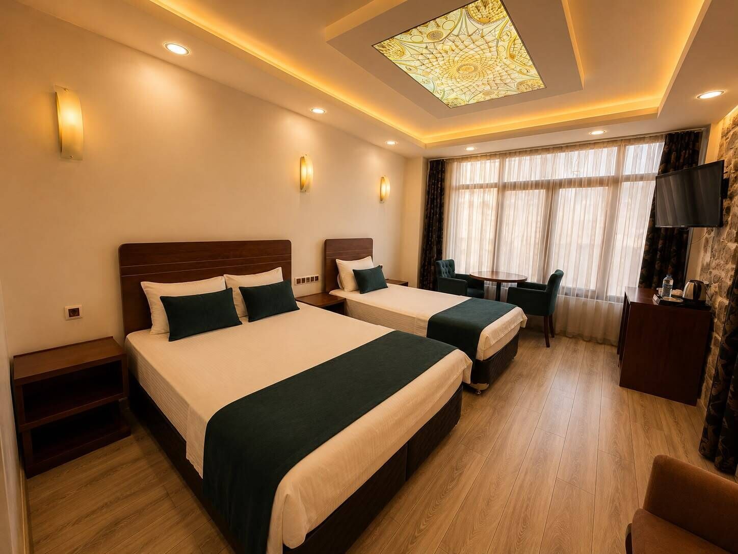 Habitación de hotel con dos camas, un escritorio, una silla, un televisor y un ventanal con cortinas.