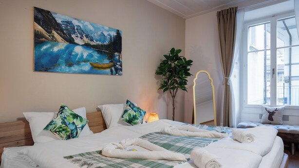 Una habitación de hotel con cama, un cuadro, una planta y una ventana.