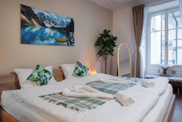 A hotel room with a bed, a painting, a plant, and a window.