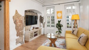 Una sala de estar con sofá, televisión, mesa y ventana con cortinas.