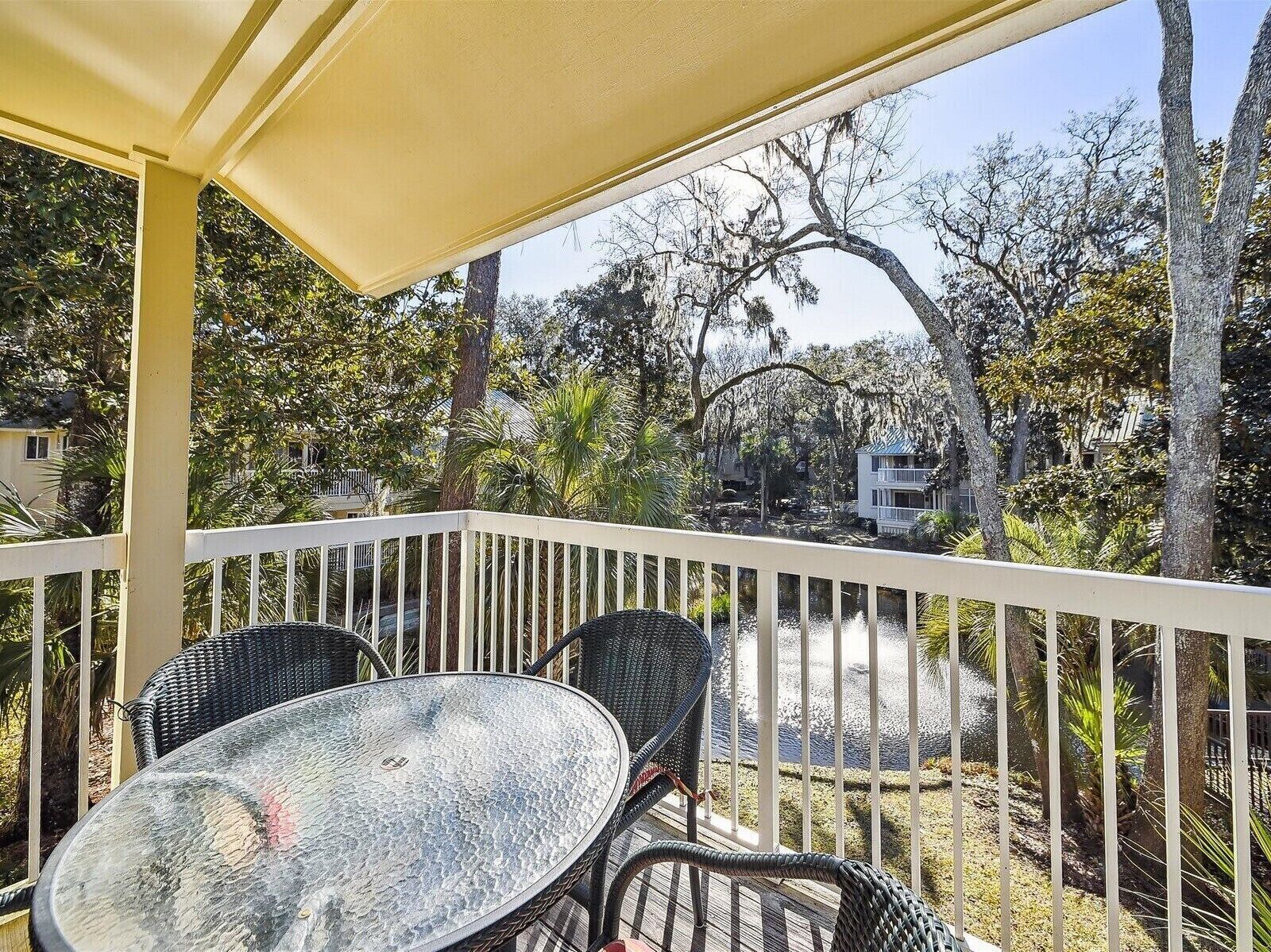 Un balcon agrémenté d’une table et de chaises, entouré d’une balustrade blanche, d’où l’on peut admirer un plan d’eau et des arbres.
