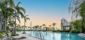A swimming pool with lounge chairs, palm trees, and modern buildings in the background. - Cozy 1-bedroom condo in lovely Kuala Lumpur with AC (Kuala Lumpur)