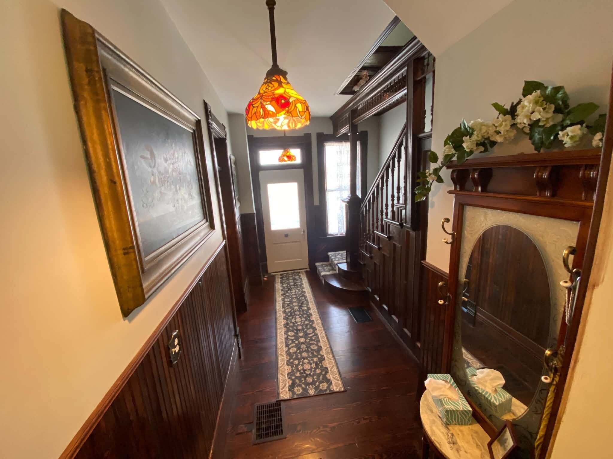 A hallway with a patterned rug, wooden doors, a staircase, and a decorative light fixture.