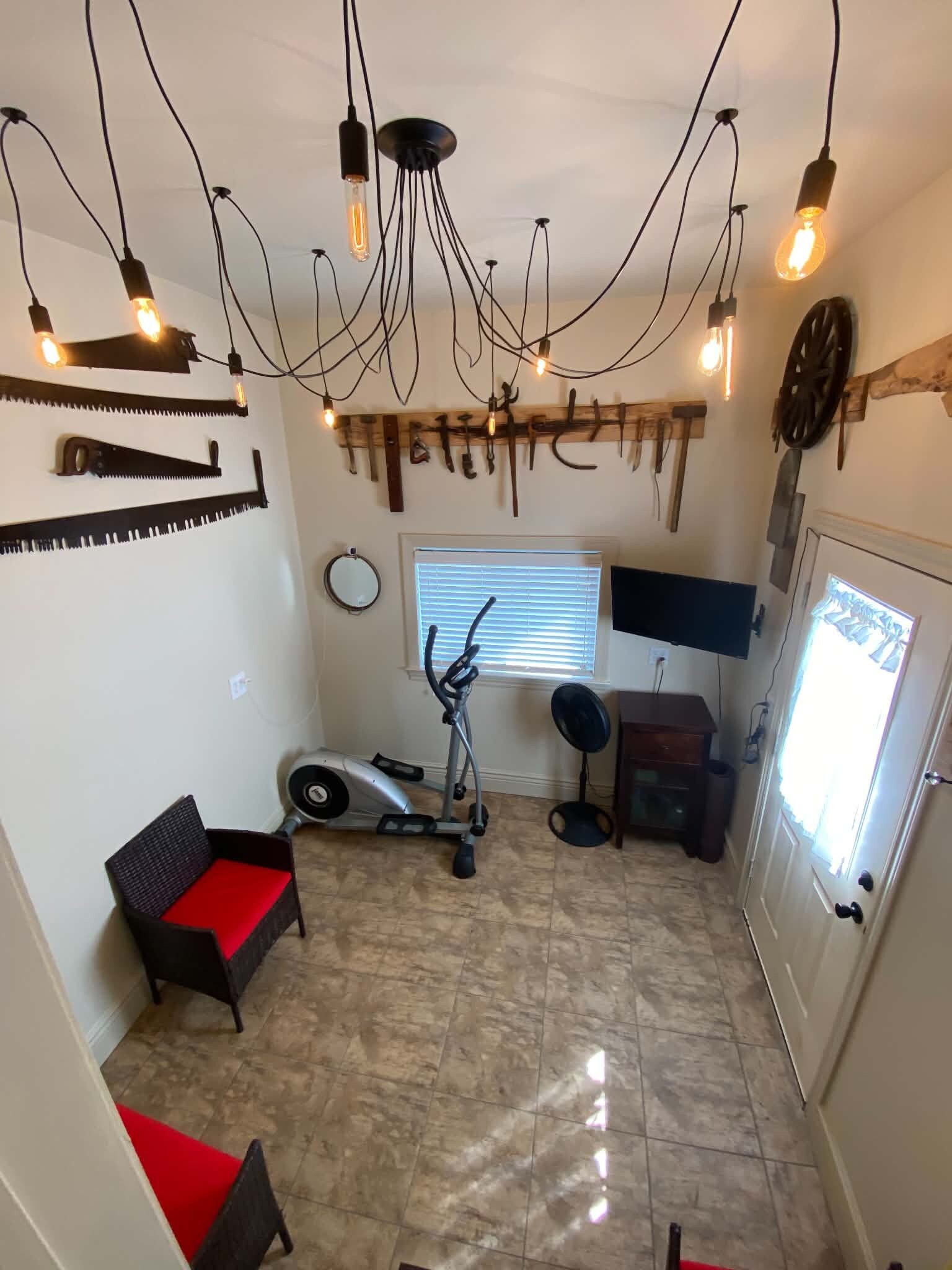 Een kamer met een plafondlamp, fitnessapparatuur, een televisie en een deur.
