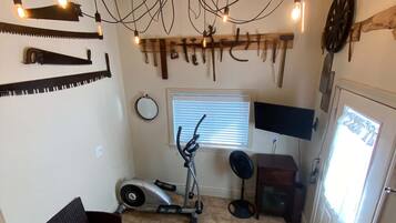 Een kamer met een plafondlamp, fitnessapparatuur, een televisie en een deur.
