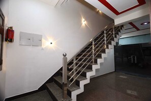 Una escalera con barandilla de metal, un extintor en la pared y una lámpara.
