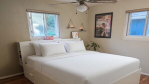 Un dormitorio con cama, ventilador de techo, dos ventanas y estantes en la pared.