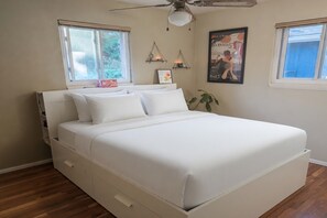 Ein Schlafzimmer mit einem Bett, Deckenventilator, zwei Fenstern und Wandregalen.