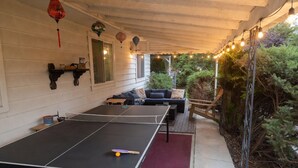 Mesa de ping pong exterior con red, rodeada de asientos exteriores y guirnaldas de luces.