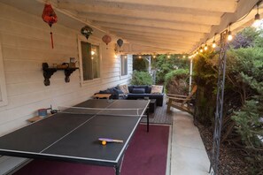 Ein Tischtennis-Tisch im Freien mit Netz, umgeben von Sitzgelegenheiten und Lichterketten.