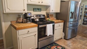 Una cocina con gabinetes blancos, una estufa de acero inoxidable, un refrigerador y una cafetera.