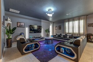 A modern living room with a large flat-screen TV, a sofa set, a coffee table, and a ceiling light fixture. - Star Wars Immersive Home w/ Private Pool, Arcade, Theater, Themed Bedrooms (Kissimmee)
