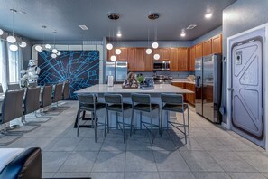 A modern kitchen with a central island, bar stools, wooden cabinets, stainless steel appliances, and a wall with a blue geometric design. - Star Wars Immersive Home w/ Private Pool, Arcade, Theater, Themed Bedrooms (Kissimmee)