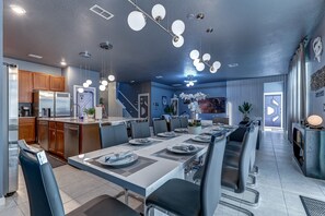 A modern kitchen with stainless steel appliances, a dining area with a long table and chairs, and a staircase leading to another level. - Star Wars Immersive Home w/ Private Pool, Arcade, Theater, Themed Bedrooms (Kissimmee)