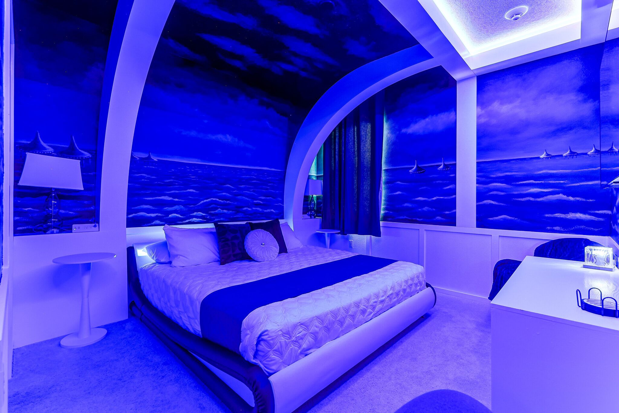 Ein Schlafzimmer mit Bett, Wandgemälde des Nachthimmels und Schreibtisch mit Lampe.