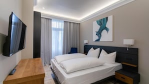 A hotel room with a bed, a TV, a desk, a nightstand, and a painting on the wall.