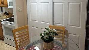 A kitchen with wooden cabinets, a microwave, and a stove. There is a dining table with chairs and a glass-top table.