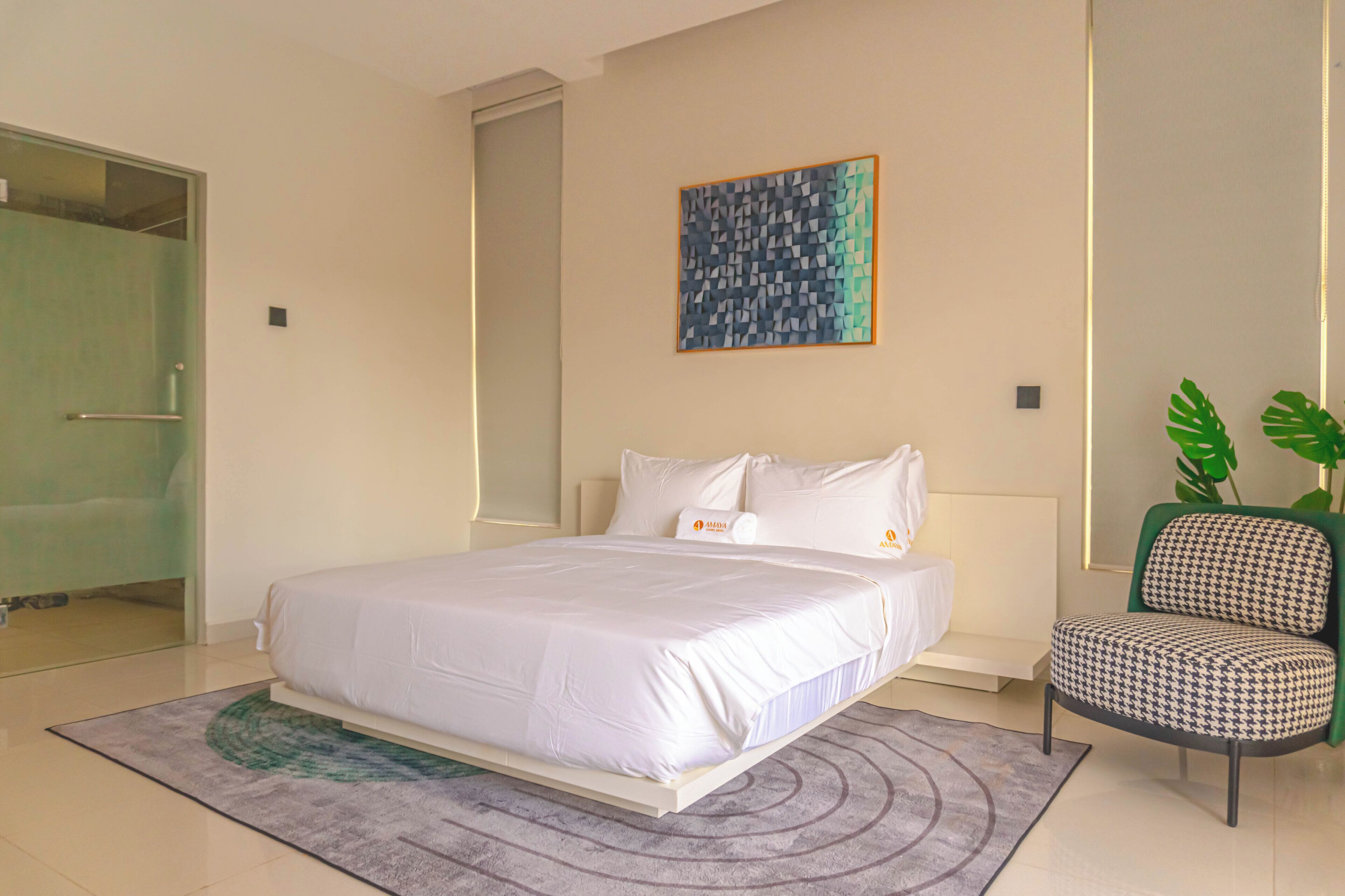 A modern hotel room with a large bed, a green chair, and a painting on the wall.