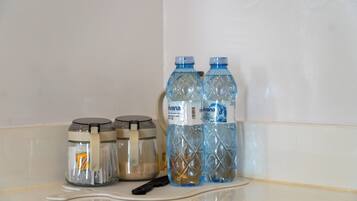 Une salle de bain avec un mur recouvert de carreaux blancs, deux bocaux en verre avec des couvercles et deux bouteilles d’eau sur une étagère blanche.