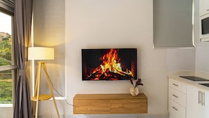 Une chambre moderne avec un téléviseur fixé au mur, un meuble en bois, un lampadaire et une fenêtre avec des rideaux.