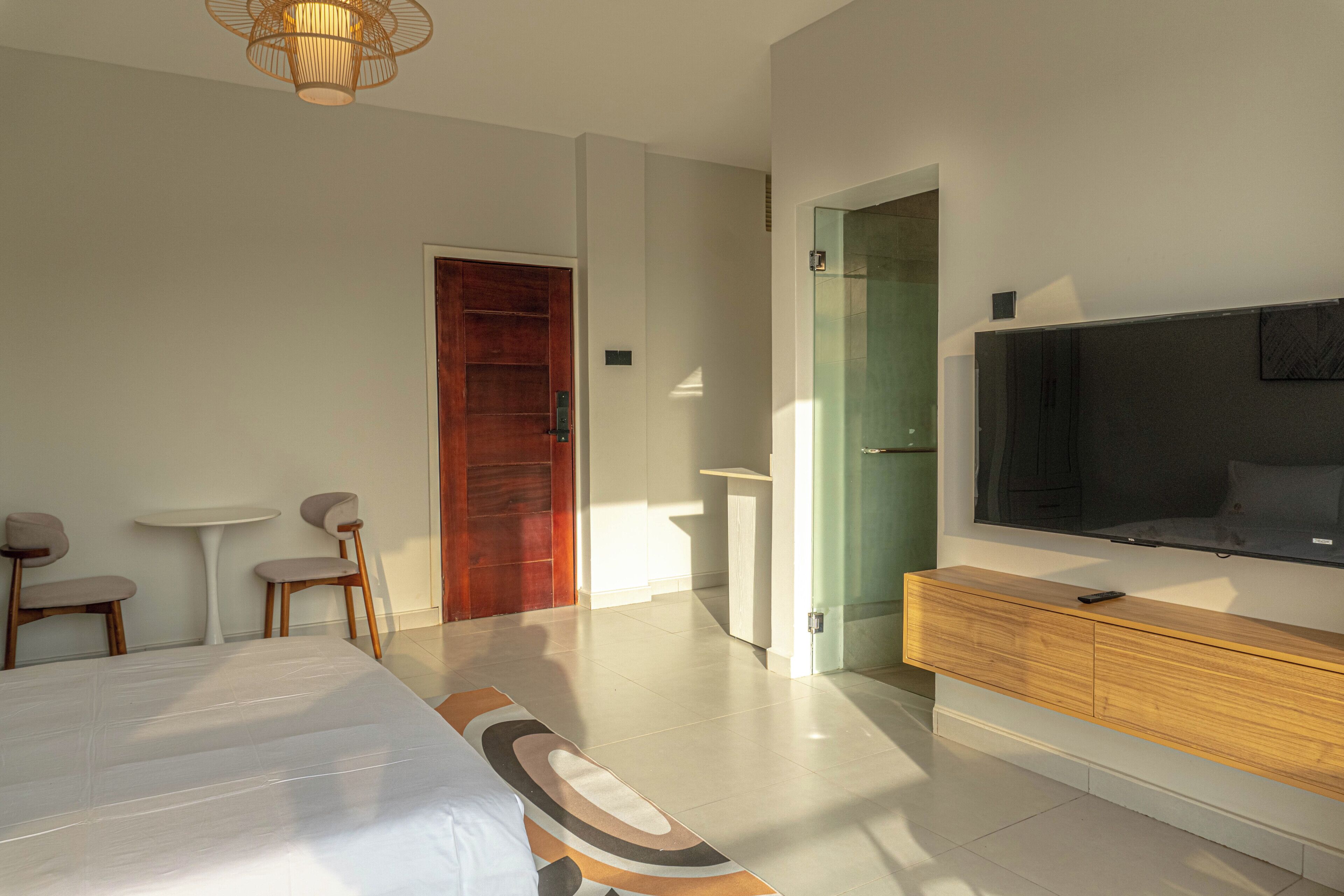 A modern hotel room with a bed, a TV, a wooden dresser, and a small table with chairs.
