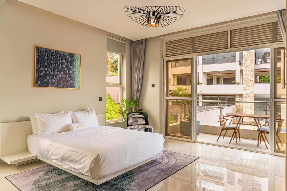 A bedroom with a bed, a window, a chair, and a balcony with a table and chairs.