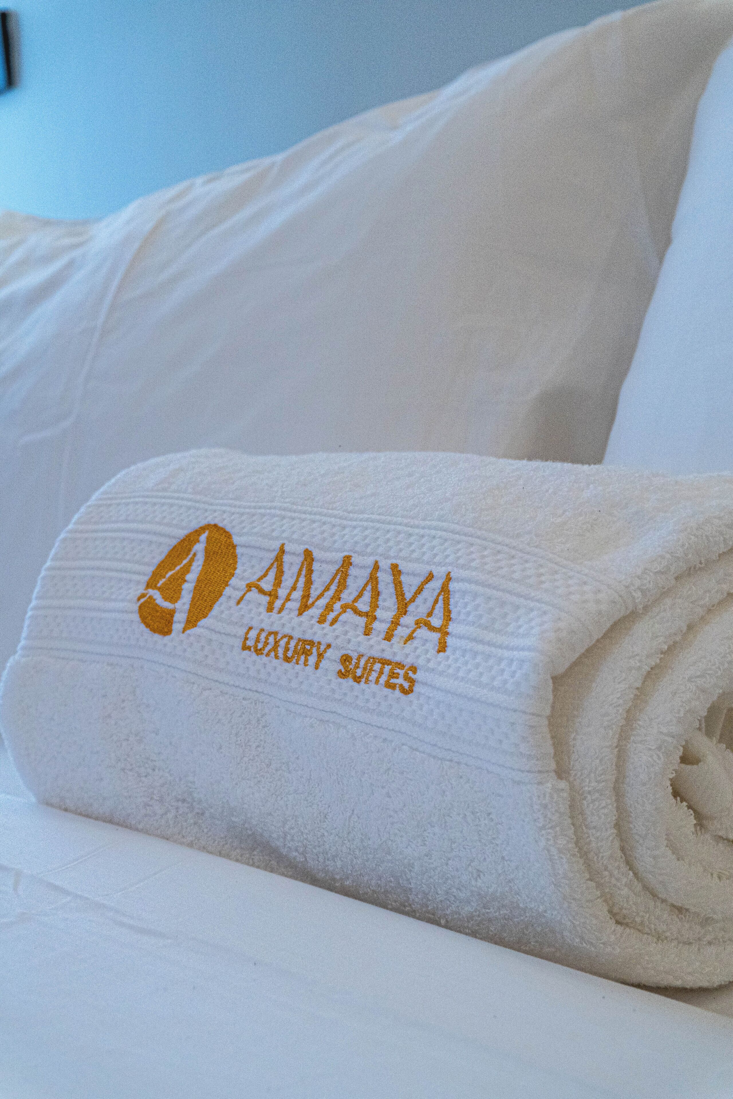 Una toalla blanca doblada con el nombre 'AMAYA LUXURY SUITES' bordado, sobre una cama.
