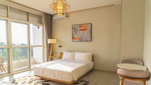 Une chambre d’hôtel avec un lit, une chaise, une petite table, une fenêtre avec des stores et un luminaire au plafond.